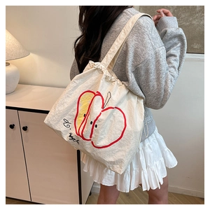 Detail of a cream canvas tote bag featuring cute red apple print and soft fabric texture