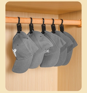 Detailed view of black plastic hooks holding five grey baseball caps in a wooden wardrobe