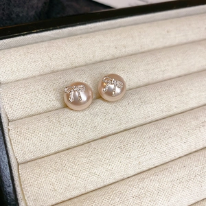 Macro shot of faux pearl earrings with silver bow design on a beige velvet jewelry box