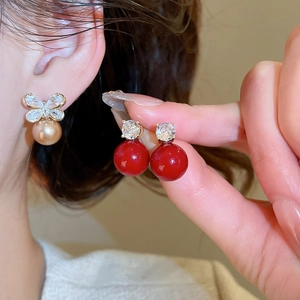 Detail of bow-shaped earring with champagne pearl and red bead drop earring