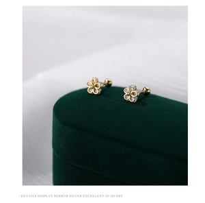 Macro shot of gold flower stud earrings with sparkling zircons on green velvet