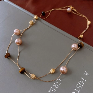 Detail of layered gold chain necklace featuring tiger eye beads and pink pearls