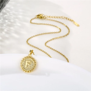 Detail of gold circular pendant with letter F and beaded edge on lobster clasp chain