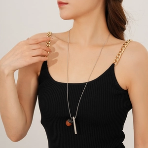 Close-up of a silver chain necklace with a dark brown acorn and metal cylinder pendant