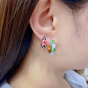 Detail view of colorful enamel camellia C-shaped hoop earrings on model with gold finish
