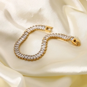 Dettaglio di bracciale in acciaio dorato con zirconi rettangolari su seta bianca lussuosa