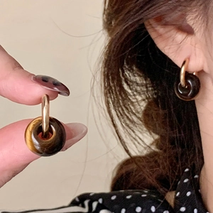 Gros plan de boucles d'oreilles créoles dorées avec pendentif en pierre oeil de tigre brun