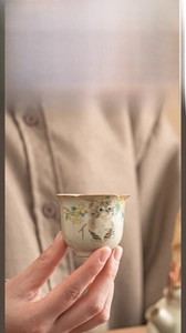 Close-up of a Ru Kiln ceramic teacup with cat and floral painting held by hand