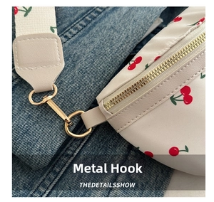 Detail of gold metal hook and zipper on white waist bag with red cherry pattern print