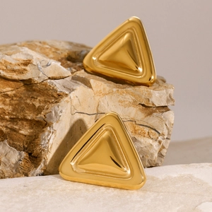 Detail von goldenen Dreieck-Ohrringen auf strukturiertem Stein mit Spiegelglanz