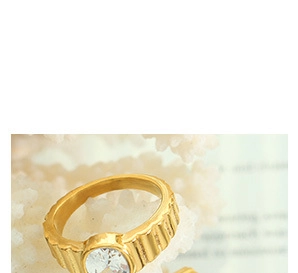 Detailed macro view of a gold ribbed ring with a round clear gemstone on coral background
