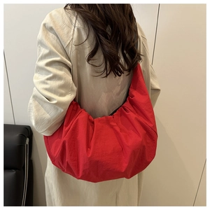 Vue détaillée du sac croissant plissé rouge porté à l'épaule par un modèle