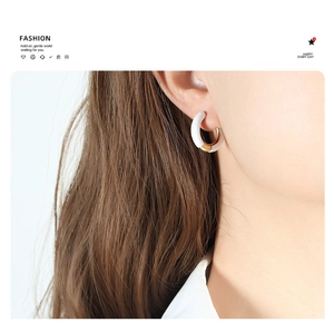 Close-up of elegant gold and white enamel hoop earrings worn on a model's ear