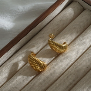 Macro detail of golden croissant earrings with spiral texture on jewelry box display