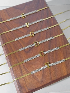 Detail of 18K gold-plated initial pendants with rectangular cubic zirconia on wooden stand