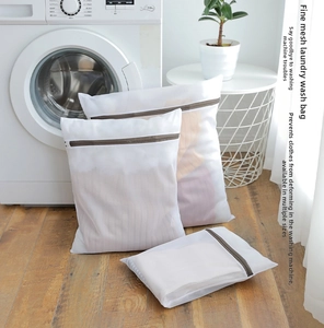 Three assorted sizes of fine mesh laundry bags with brown zippers on a wooden floor
