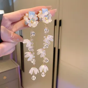 Detail of silver needle earrings featuring blue gemstone, white flower and crystal tassel