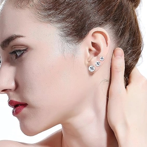 Close-up of three sizes of silver round zircon stud earrings worn on a model's ear