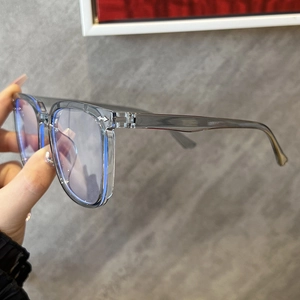 Detail showing transparent grey square glasses frames held against a textured wall