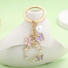 Close-up of gold keyring with enamel sakura and butterfly charms plus a white pearl