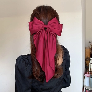 Detail of wine red satin bow hair clip on model with long brown hair and black top