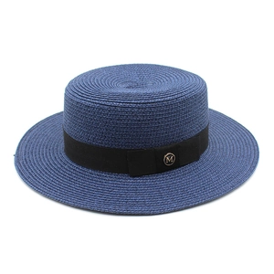Détail d'un chapeau de paille bleu marine avec ruban noir et emblème logo M doré