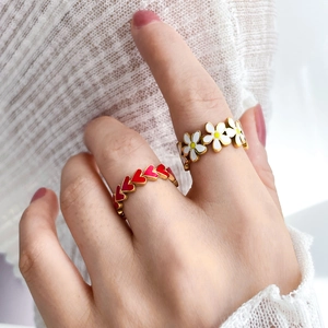 Detail of gold rings featuring red enamel hearts and white daisy flowers on hand