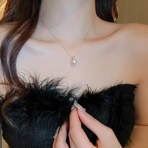 Detailed view of a gold pearl necklace with zircon accents worn on a woman neck