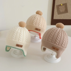 Detail of baby cable knit hats with cozy pom-poms and leather logo labels in autumn tones