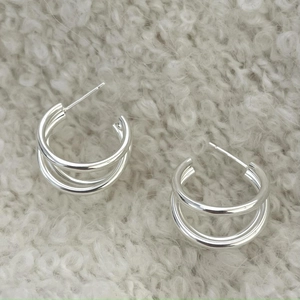Detailed view of silver S925 multi-layered C-shaped hoop earrings on grey knit background