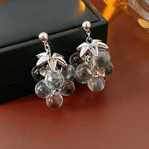Close-up of crystal grape tassel earrings with silver leaves on brown leather texture