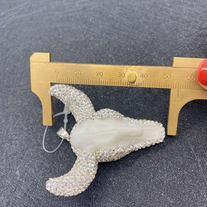 Macro shot measuring a white acrylic bull head pendant with rhinestones using a brass caliper