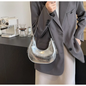 Detail of silver crescent shoulder bag with metallic mirror finish in a cafe setting