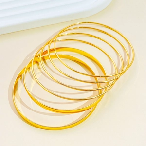Close-up of minimalist gold polished bangle set on a white textured decorative tray