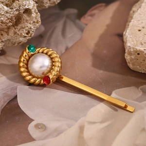 Detailed macro of 18K gold twist hair clip with large pearl and colorful gemstones
