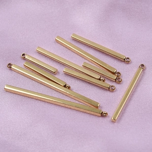 Close-up of gold bar pendants with ring holes on pink silk for DIY jewelry making