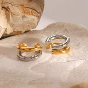 Polished dual-tone stainless steel ear cuffs in gold and silver finish on a stone surface