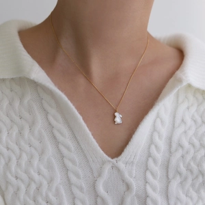 Collier en acier titane doré avec pendentif lapin en nacre blanche sur pull blanc