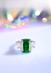 Macro view of emerald-cut green gemstone with side stones in silver four-prong setting