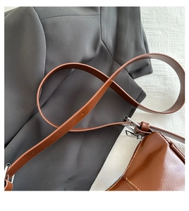 Detailed view of brown leather crescent bag texture with silver metal buckles on gray blazer