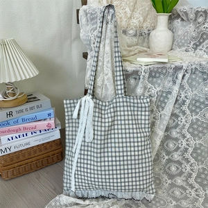 Detail of black and white plaid tote bag featuring delicate white lace trim and bow ribbons