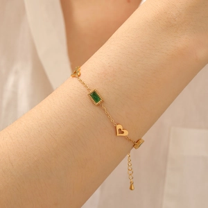 Detailed close-up of a gold-plated bracelet featuring a hollow heart and green gemstone