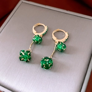 Close-up of gold earrings with green faceted spheres on a grey jewelry box cover