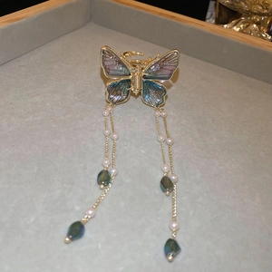 Detail of golden butterfly hair claw with iridescent purple wings and pearl tassels