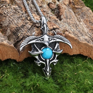 Vintage stainless steel eagle wing pendant with turquoise stone on a wooden backdrop
