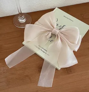 Close-up of a large pale pink chiffon bow hair clip on a vintage book and wooden table
