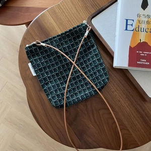 Detail of green tweed crossbody bag with leather strap on a rustic wooden table