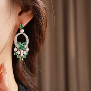 Détail de boucles d'oreilles pendantes avec pierres vertes et pompons argentés
