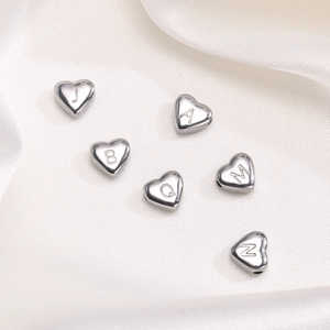Detailed view of silver heart-shaped stainless steel beads with engraved letters on silk