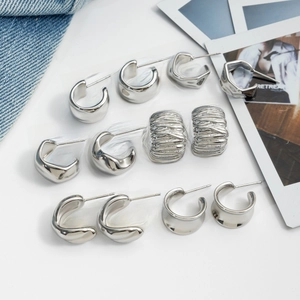 Flat lay of minimalist silver C-shaped earrings and irregular geometric studs on denim